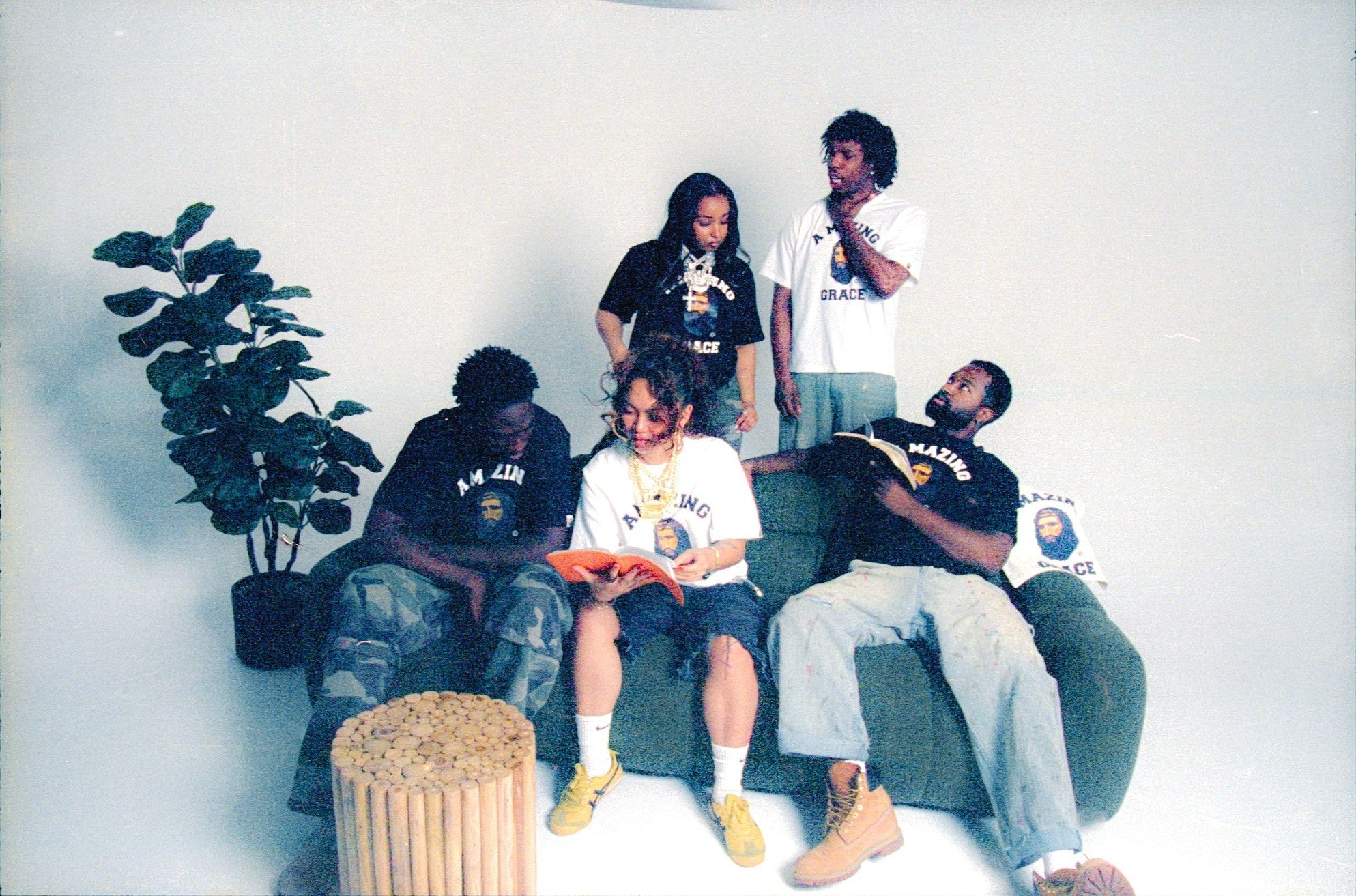 Five people sitting on a couch with a plant and a stool in the foreground.